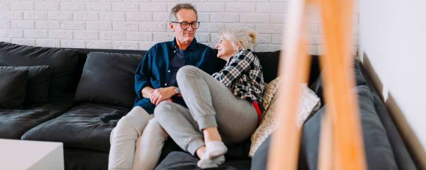 Älteres Paar sitzt entspannt gemeinsam auf dem Sofa und blickt sich an – eine Alltagsszene, die das Thema private Altersvorsorge und finanzielle Planung im Alter aufgreift.