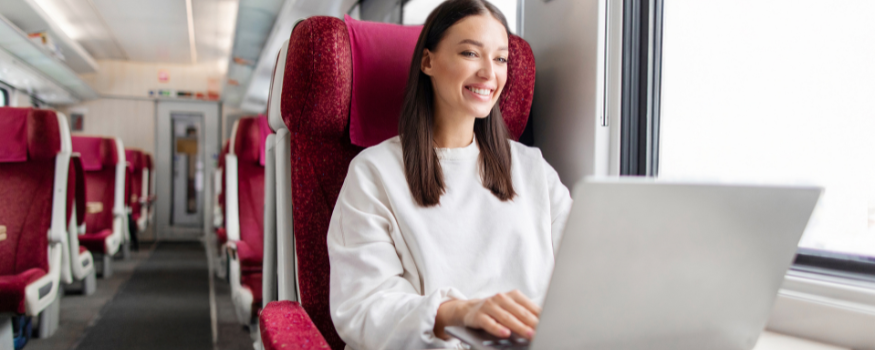 Frau mit Laptop arbeitet im Zug am Fensterplatz – Beispiel für bezahlte Arbeitszeit auf Dienstreisen, wenn während der Fahrt gearbeitet wird. Symbolbild zur Frage, welche Tätigkeiten zur vergütungspflichtigen Arbeitszeit zählen.