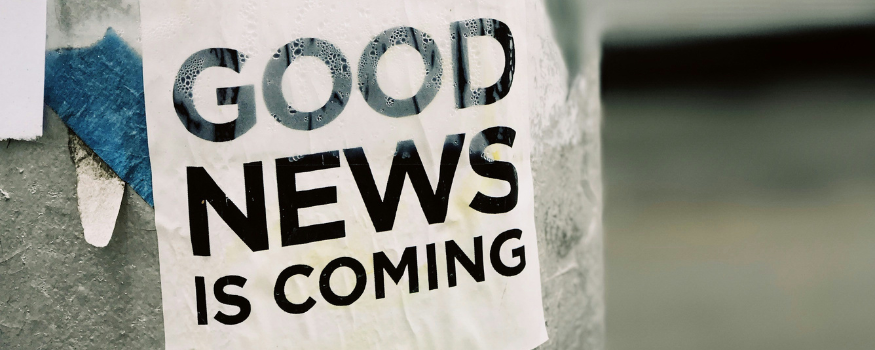 Plakat mit der Aufschrift „GOOD NEWS IS COMING“ an einer grauen Wand, als positive Ankündigung für steuerliche Entlastungen und Investitionsförderungen im Rahmen des Investitionswachstumspakets 2025.