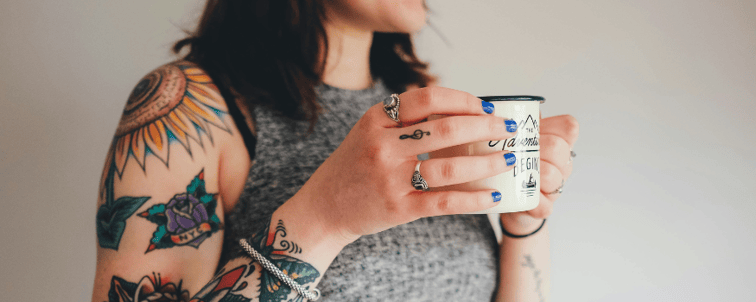 Junge Frau mit frischem Tattoo an Arm und Hand hält eine Tasse. Die Szene symbolisiert den Anlass eines arbeitsrechtlichen Falls: Nach Entzündung ihres neuen Tattoos fiel eine Mitarbeiterin krankheitsbedingt aus – und erhielt keine Lohnfortzahlung, da das Gericht von Selbstverschulden ausging.